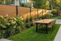 Moderne houtlook schutting van premium houtcomposiet met zwarte aluminium palen in een strak ingerichte tuin met houten eettafel en hortensia's.