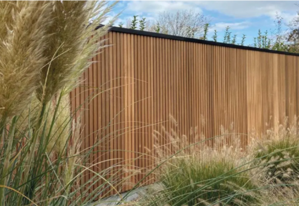 Luxe Bardot tuinscherm in thermowood ayous met een modern verticaal ribprofiel en zwart aluminium afwerking.