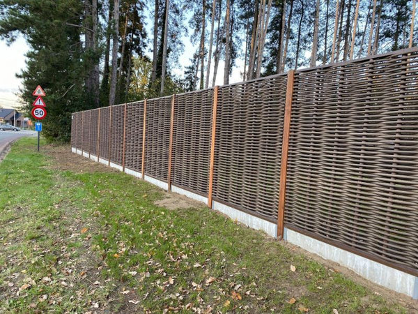 Forest Avenue gevlochten tuinscherm van kunststof fiber in een natuurlijke bruine kleur, geplaatst op een betonplint langs een bosrand.